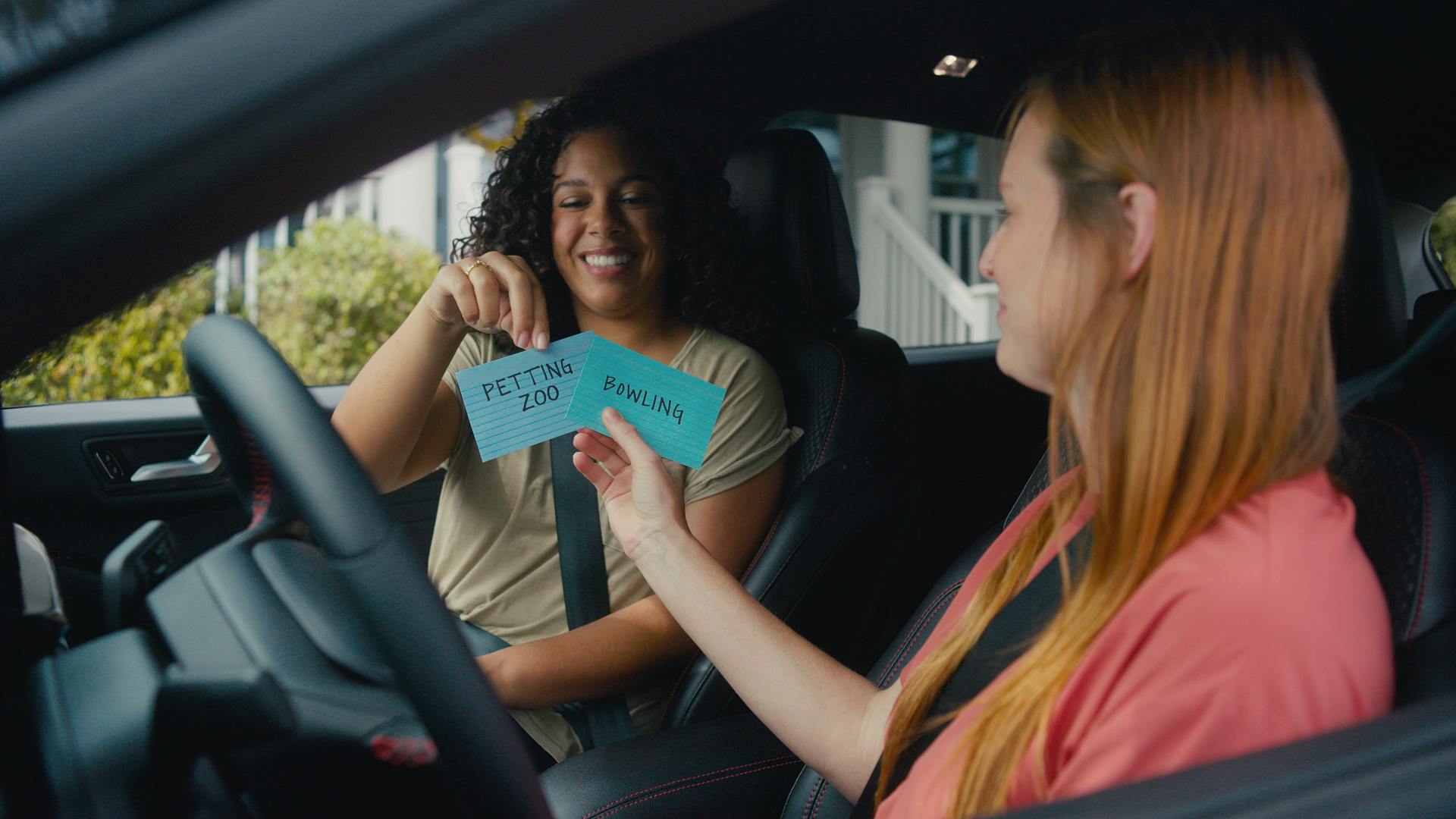 Two girls in a Ford Escape SUV picking between index cards that say "Petting Zoo" and "Bowling"