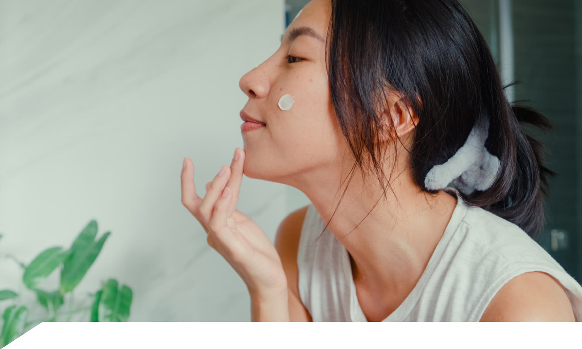 A woman with face cream on her cheek and her hand touching her chin
